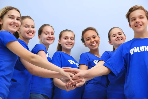 Team von Freiwilligen, die ihre Hände als Symbol der Einheit zusammenlegen, auf farbigem Hintergrund — Stockfoto