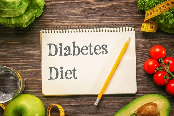 Notebook with text DIABETES DIET and healthy food on wooden background. Health care concept