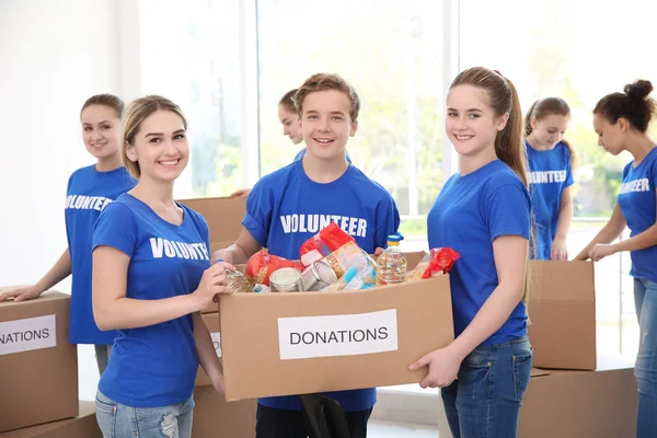 Young volunteers with box of donations indoors — Stock Photo, Image