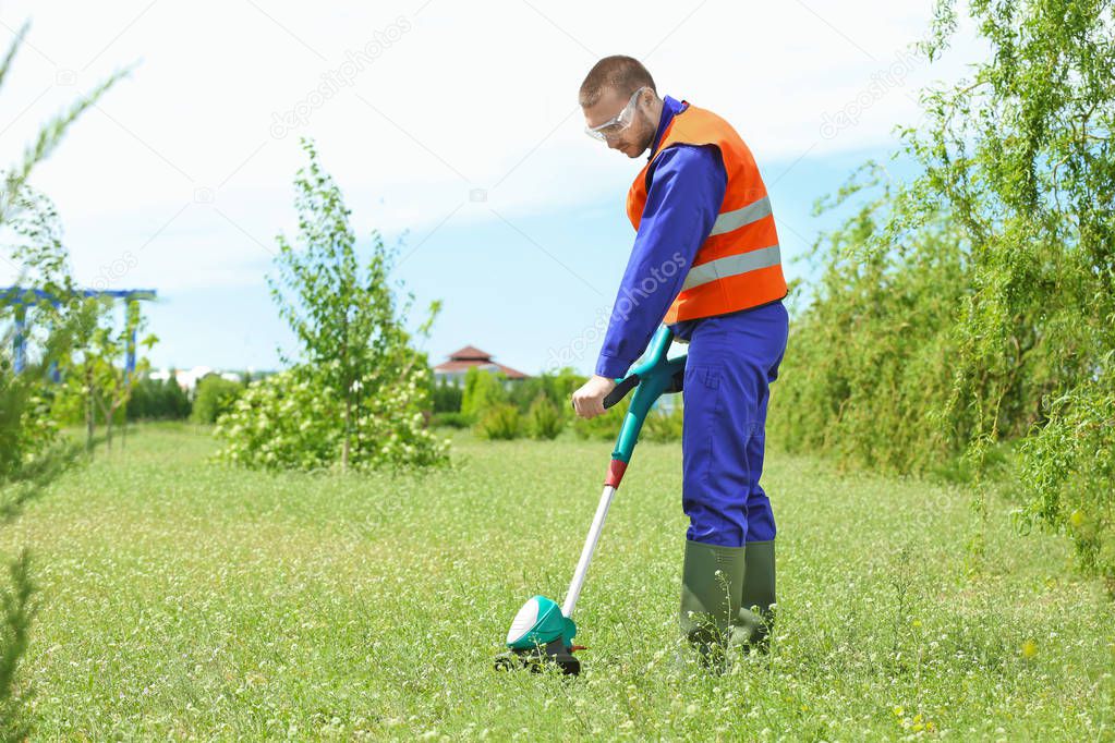 worker mowing lawn with grass trimmer 