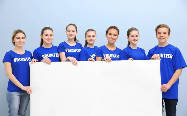 Group of young volunteers with poster on color background — Stock Photo, Image