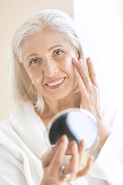 Anciana aplicando crema facial — Foto de Stock