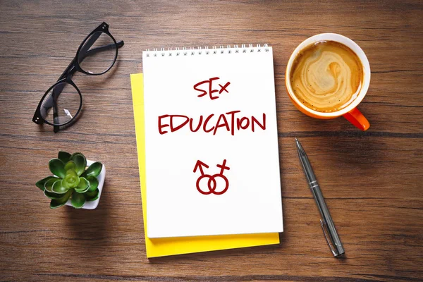Sex education concept. Notebook with glasses and cup of coffee on wooden background — Stock Photo, Image