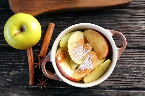Tureen avec morceaux de pomme fraîche, sucre en poudre et cannelle sur table en bois foncé — Photo