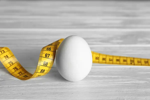 Яйцо с измерительной лентой на деревянном столе — стоковое фото