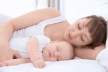 Evde yatakta yatarken şirin uyuyan bebek olan kadın
