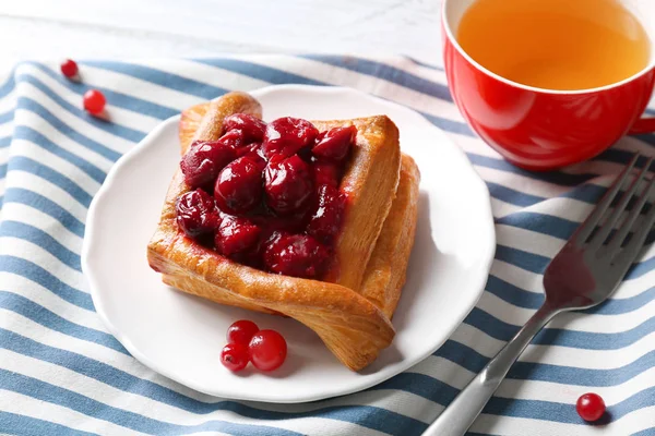 Plate with puff and cherry on striped napkin — Stock Photo, Image