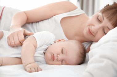 Evde yatakta yatarken şirin uyuyan bebek olan kadın