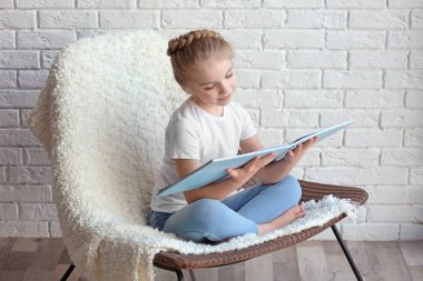Kitap ile sandalye üzerinde oturan küçük kız