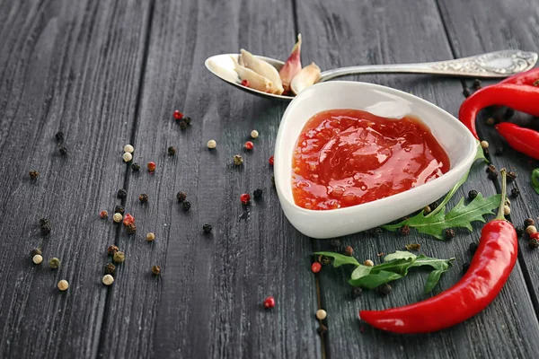 Compoziția sosului de chili gustos în castron și ingrediente pe masa de lemn — Fotografie, imagine de stoc