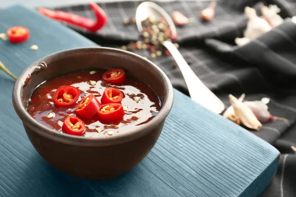 Вкусный соус чили в миске на деревянной доске — стоковое фото