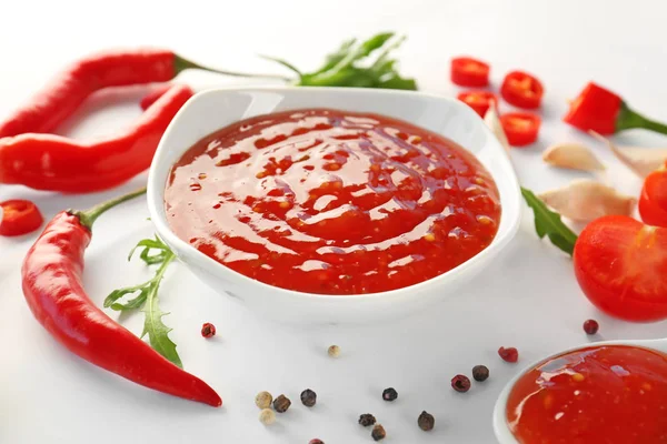 Sabrosa salsa de chile en tazón e ingredientes sobre fondo blanco — Foto de Stock