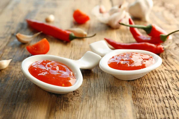 Tasty chili sauce in spoons on wooden table