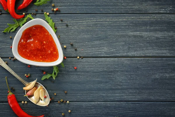 Composition of tasty chili sauce in bowl and ingredients on wooden table — Stock Photo, Image