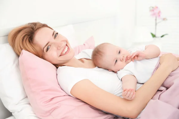 幸福的年轻女人，与可爱的宝宝躺在家里的床上 — 图库照片