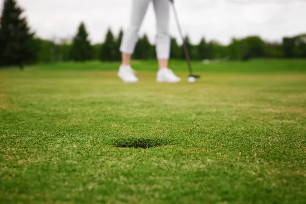 Groene golfbaan met gat en wazig jonge vrouw op achtergrond — Stockfoto