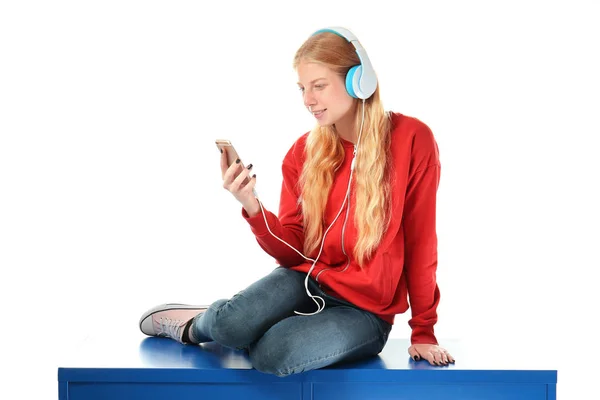 Linda chica adolescente con teléfono móvil y auriculares escuchando música sobre fondo blanco — Foto de Stock