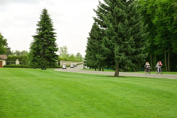 Сучасні візки для гольфу, що рухаються по дорозі біля зеленої траси — стокове фото