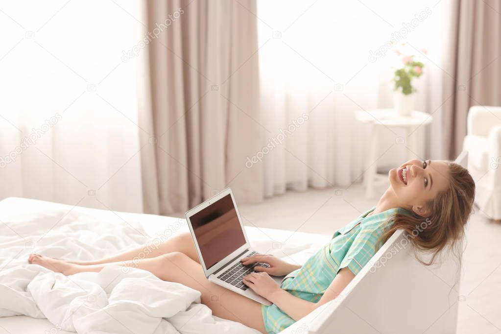 Morning of beautiful young woman sitting on bed with laptop
