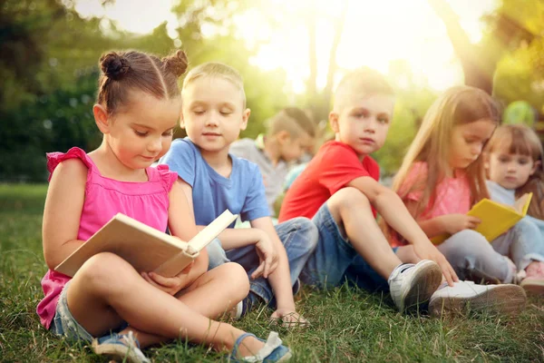 Niños lindos leyendo libros en el parque. Concepto vacaciones escolares —  Fotos de Stock