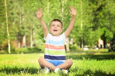 Sevimli küçük çocuk parkı yeşil çimenlerin üzerinde oturan