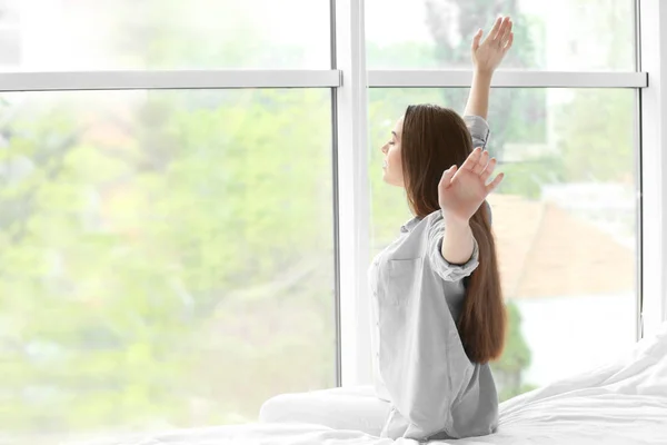 Mladá žena, táhnoucí se po spánku proti okno — Stock fotografie