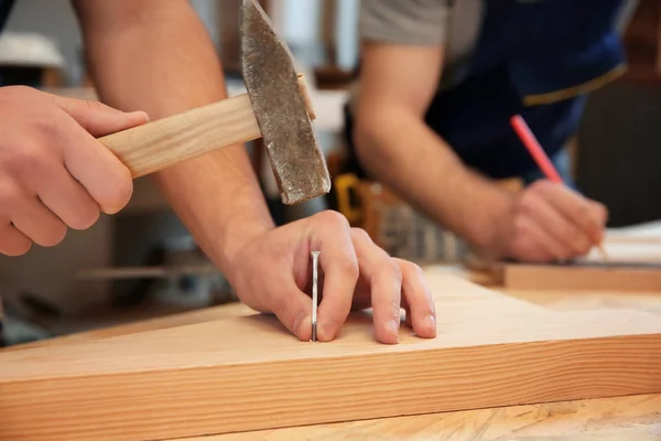 Carpenter jízdy hřebík do dřevěné desky v dílně, closeup — Stock fotografie