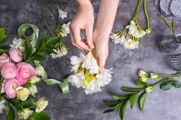 Female florist making beautiful bouquet with freesia flowers on gray background — Stock Photo, Image