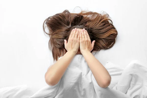 Молодая женщина лежит в постели и закрывает лицо руками — стоковое фото