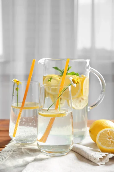 Tillbringare och glasögon med uppfriskande citronvatten på träbord — Stockfoto