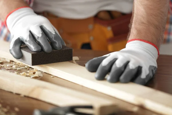 Carpenter sanding wooden plank on table, closeup — Stock Photo, Image