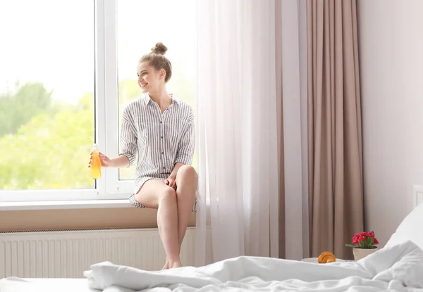Sabah güzel genç kadının evde pencere pervazına üzerinde otururken suyu içme — Stok fotoğraf