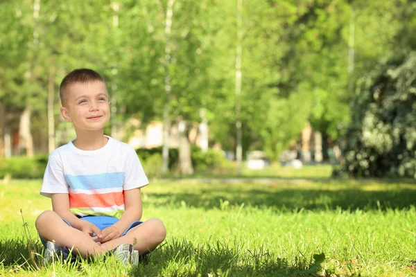 Anak kecil yang lucu duduk di rumput hijau di taman — Stok Foto