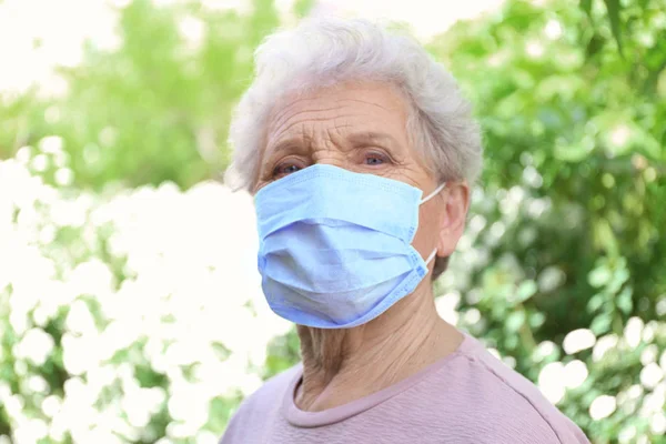 Mujer mayor que usa mascarilla entre los arbustos florecientes. Concepto de alergia — Foto de Stock