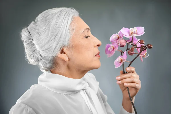 Mulher idosa bonita com flores de orquídea — Fotografia de Stock