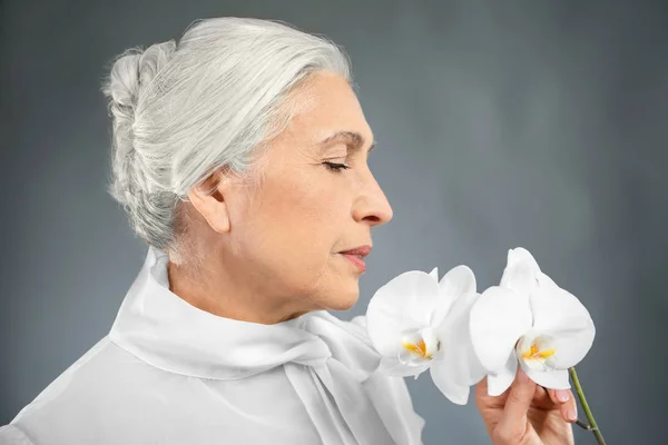 Mulher idosa bonita com flores de orquídea — Fotografia de Stock