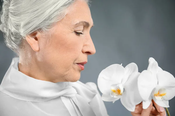 Mulher idosa bonita com flores de orquídea — Fotografia de Stock