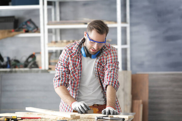 Carpenter sanding wooden plank on table 