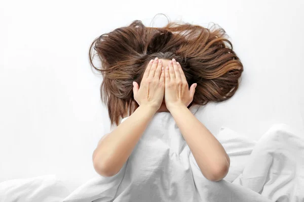 Mujer joven acostada en la cama y cubriendo la cara con las manos Imagen de archivo