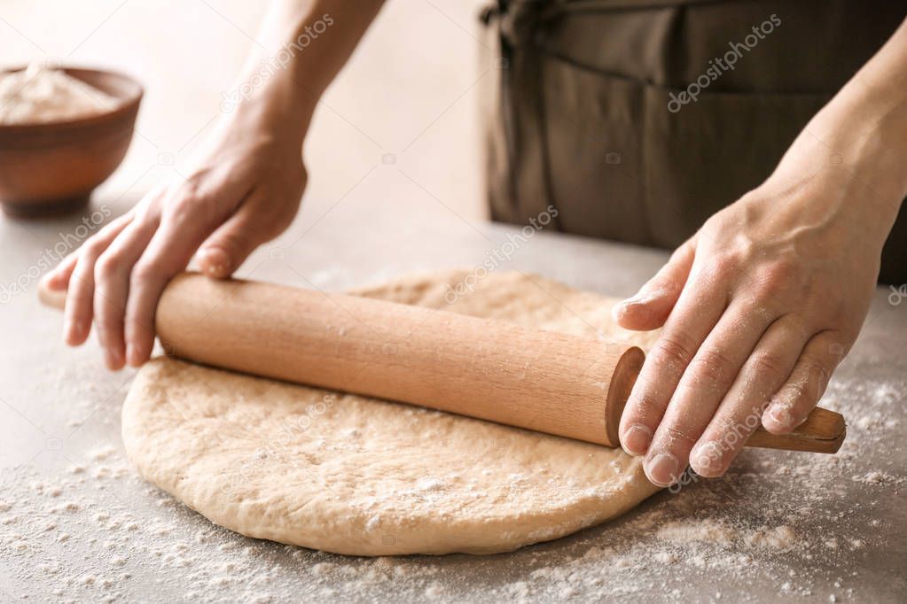 Woman rolling dough for cinnamon rolls on kitchen table