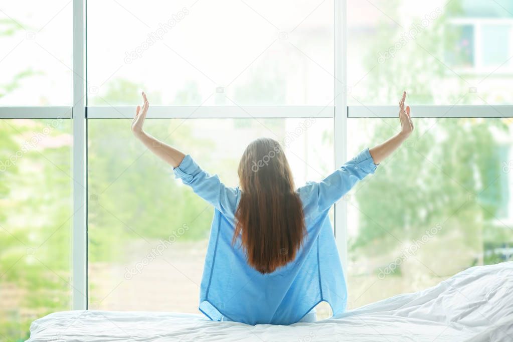 Young woman stretching after sleep against window