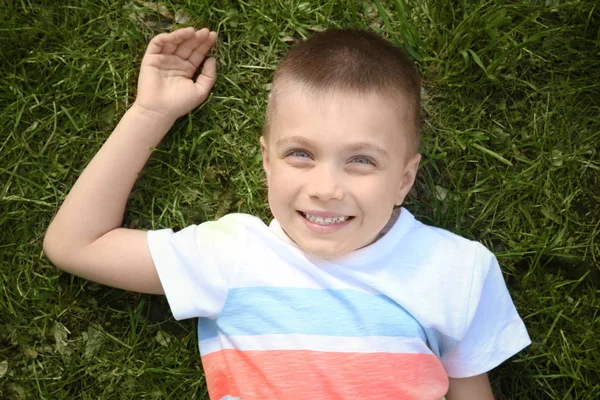 Cute little boy lying on green grass in park Stock Picture