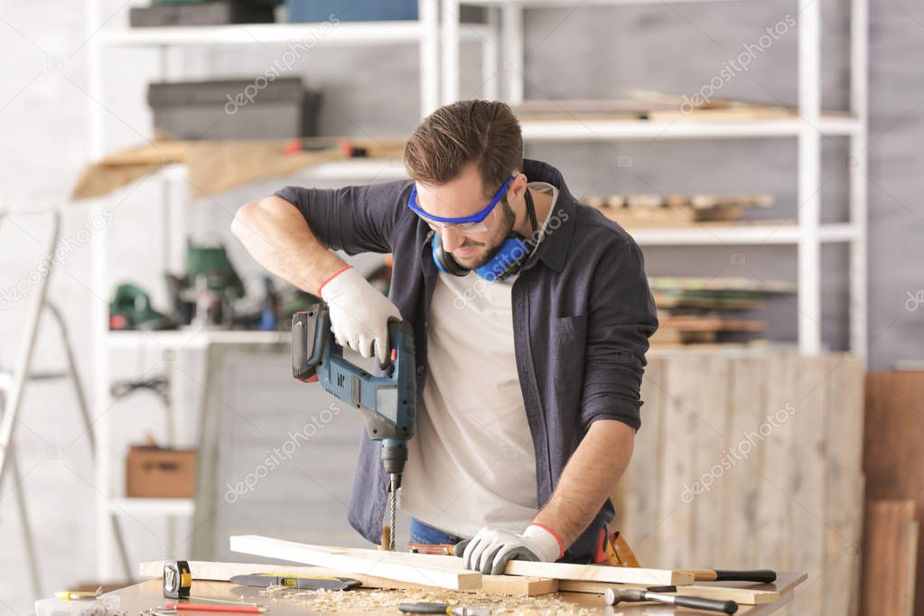Young carpenter drilling wooden plank