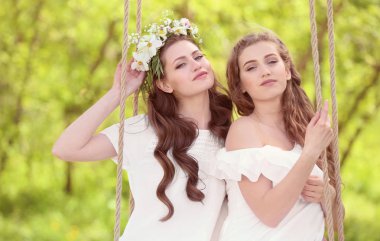 Two beautiful young women on swing in park clipart