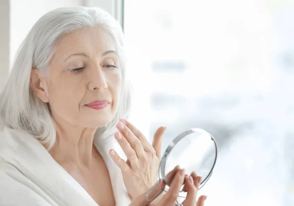 Mulher idosa aplicando creme facial — Fotografia de Stock