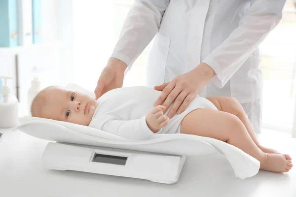 Doctor examining baby on scales in room — Stock Photo, Image