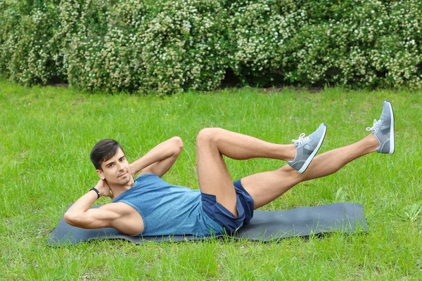 Atlético jovem fazendo exercício de bicicleta crunch enquanto deitado no tapete ao ar livre — Fotografia de Stock