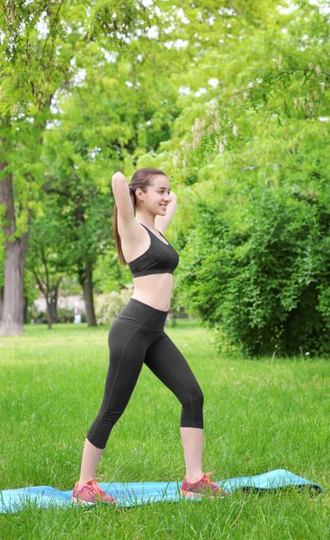 Atletische jonge vrouw doen fiets crunch oefening staand op mat in groene lente park — Stockfoto