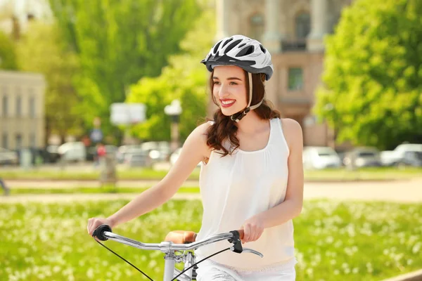 Mooie jonge vrouw met fiets en helm in park op zonnige dag — Stockfoto