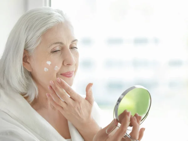 Anciana aplicando crema facial — Foto de Stock